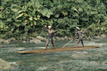 Two Embera boys using pole to steer wooden dug out canoe through fast flowing rapids.  Young boys adept at using canoes from very early age  wear crowns of wild sweet-smelling lilies to attract girls...