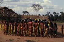 Panara men wearing crowns or head-dresses of feathers encircled by women painted with red karajuru and with long strips of plant fibres tied around upper arms during dance.Formally known as Kreen-Akr...