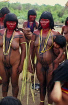 Panara women painted with red karajuru and wearing multi-strands of beads across upper body and long strips of plant fibres tied around upper arms in preparation for dance. Formally known as Kreen-Ak...