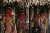 Young Panara women applying red karajuru face and body paint in preparation for dance.  Wearing multi-strand bead necklaces and long strips of plant fibres tied around upper arms. Formally known as K...