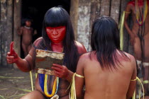 Young Panara women applying red karajuru face and body paint in preparation for dance.  Formally known as Kreen-Akrore  Krenhakarore  Krenakore  Krenakarore  Amazon American Brasil Brazilian Female W...