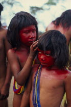 Young Panara girls applying red karajuru face and body paint in preparation for dance.  Both wearing multiple strands of blue red and yellow beads across upper body.Formally known as Kreen-Akrore  Kr...