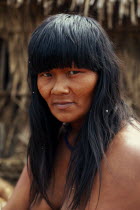 Head and shoulders portrait of young  Panara woman outside thatched home part seen behind.Formally known as Kreen-Akrore  Krenhakarore  Krenakore  Krenakarore  Amazon American Brasil Brazilian Female...
