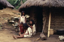 Kogi-Wiwa family outside mud-wattle/grass thatched home in Avingue village on South side of Sierra Nevada de Santa Marta. Mother de-lousing grandmothers hair. Strings of red glass beads a sign of fami...