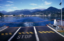View across Lake Maggiore towards shoreline and Pallanza from the ferry with warning Stop sign on ferry deck in foreground and rope across end.