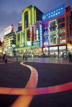 Nanjing Lu.  Busy street scene at night with illuminated neon signs and advertising and ribbon of pink / orange lit pavement across square in the foreground.
