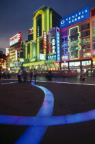 Nanjing Lu.  Busy street scene at night with illuminated neon signs and advertising and ribbon of blue lit pavement across square in the foreground.
