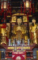 Yu Gardens  Temple of the City of God.  Three golden statues behind small altar with candles and incense and decorated lanterns hanging above.