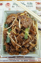 Rectangular dish of seseme pork with pair of chopsticks lying across top corner.