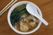 Wonton soup.  Dumplings in a vegetable broth in bowl with spoon and chopsticks.