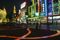 Nanjing Lu.  Busy street scene at night with illuminated shop fronts  neon signs and advertising and ribbon of lit pink / orange paving across square in foreground.