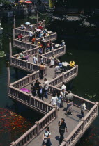 Yu Gardens.  View over zig-zag foot-bridge over pond with mass of silver and orange Koi carp. Vendors and crowds smoking  sightseeing and posing for / taking photograhs