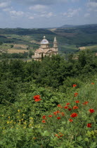 Tempio di San Biagio Church. High Renaissance church with domed roof surrounded by lush green trees and red poppies growing in the foreground