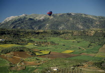 A hot air balloon flying over green valley with patchwork fields towards mountain range