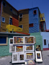 Paintings on display with colourful architecture behind