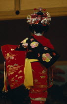 Young girl seen from behind  wearing traditional red embroidered kimono with black sash or obi and red and silver hair decoration during festival of the shrines and temples.