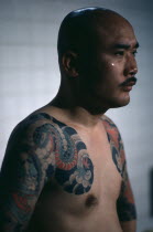 Three-quarter shot of gangster or Yakuza gang member in public bath house showing tattoo extending over shoulder and upper arm.  Tattoos are chosen to depict inspiring ideals of heroism and romance in...