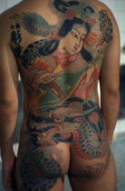 Cropped shot of heavily tattooed back of gangster or Yakuza gang member in public bath house.  Design depicts a musician and dragon.