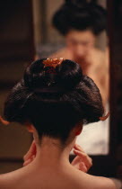 Head of geisha seen from behind to show hairstyle with mirror reflection beyond.  Wigs may be used on special occasions  but geisha and maiko usually fix their own hair into an elaborate style known a...