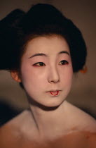 Head and shoulders portrait of sixteen year old Someiyu  a maiko or apprentice geisha with white powdered face and lips outlined in red.