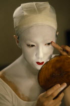 Kabuki actor Tamasaburo looking in hand mirror to apply make-up for role of Izayoi the courtesan turned crook in  The Village School .  In kabuki all female roles are played by male actors or onnagata...