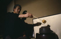 Grand Tea Master Sen Soshitsu pouring water from kettle or kama heated on charcoal burner or furo using long  stemmed bamboo ladle or hishaku.