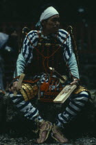 Portrait of Samurai wearing armour constructed of plates of metal or bamboo held together with coloured lacing  rope sandals and white cloth head band with sword at side.  Seated  holding bento lunchb...