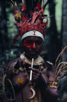 Portrait of woman wearing traditional dress and jewellery  elaborate red feather head-dress with band of white beads across forehead and  bead armlets  necklaces and fur collar and red face paint exte...