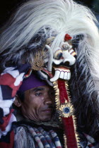 Portrait of village man with head dress topped with mask depicting the witch Rangda who epitomises evil.  He becomes possessed by the spirit of Rangda during the performance of a ritual drama.