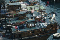 Sampan homes anchored in the harbour.  People and belongings on decks hung with washing.  Fish drying on roof of boat in foreground.