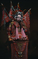 Performer in traditional Chinese opera wearing elaborate red and blue costume with dramatic black  white and red face paint.