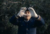 Man doing early morning T ai Chi Chuan  the ancient Chinese discipline of physical training in a small riverside park.  Face partly framed by outstretched hands.