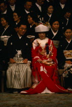 Seated bride and groom and guests attending Shinto wedding ceremony wearing traditional dress before changing into western style clothes for later party.