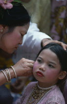 Young girl wearing make up and jewellery having her ear pierced by older woman.