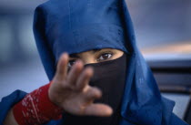 Portrait of young veiled woman reaching towards camera possibly to stop photograph being taken.