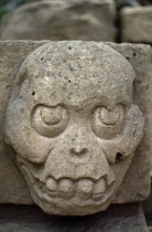 Site of ancient Mayan ruins.  Detail of carved stone skull-like face.