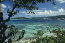 West Indies, Jamaica, Port Antonio, View across turquoise sea towards beach and tree covered coast part framed by tree branches.