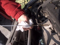 Man checking oil level on the car engine dipstick and wiping it on a white paper tissue