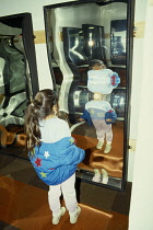 Young girl looking at her own distorted reflection in crazy mirror.