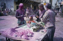 Holi Festival paint stall with people and street covered in layer of pink powder.