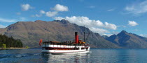 QUEENSTOWN  VINTAGE STEAMSHIP TSS EARNSALW LEAVING STEAMER WHARF AT QUEENSTOWN TAKING TOURISTS AND SAILING ON LAKE WAKATIPU WITH CECIL PEAK AND WALTER PEAK  FAR R  BEHIND.Antipodean Oceania