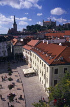 View over paved square and cafe  across red tiled rooftops of the Old Town towards Cathedral of St Martin and Bratislava Castle.