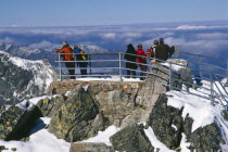 Slovakia, Carpathian Mtns, High Tatras Mtns, People at the Lomnicky Stit viewpoint with views across snowy peaks of the High Tatras mountains and drifting cloud.