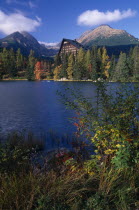 Strbske Pleso.  View across lake towards chalet and mountains beyond with surrounding trees and vegetation in Autumn colours.