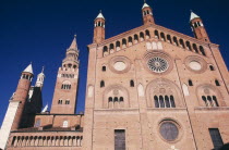 Piazza del Comune.  Southside exterior of the Duomo and bell tower or Torrazzo.  Red brick with circular and arched windows and multiple spires.