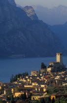 Malcesine.  View across town rooftops towards Castello Scaligero in warm  golden light with lake and mountains beyond.