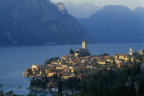 Malcesine.  View across town rooftops towards Castello Scaligero in warm  golden light with lake and mountains beyond.