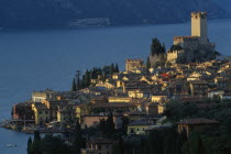 Malcesine.  View across town rooftops towards Castello Scaligero in warm  golden light with lake beyond.