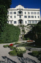 Tremezzo.  Exterior facade and formal gardens of the Villa Carlotta.  Gravel pathway encircling fountain with tiered steps leading to entrance behind.