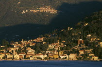 Torno.  View across Lake Como towards town spread across hillside in golden sunlight.